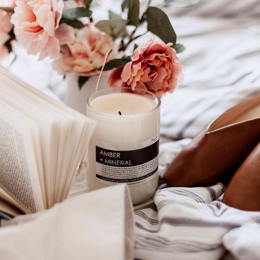 Candle on a bed next to an open book and a vase of flowers